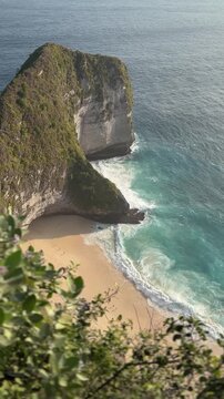 Aerial view of a rocky coastline with a sandy beach and turquoise waves. Lush greenery frames the scene, highlighting the natural beauty of the landscape.