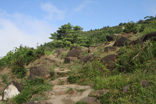 Rocky mountain hiking trail surrounded by lush green slopes and blue sky on Mount Tsukuba, Japan.   