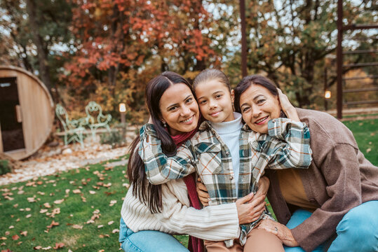 Mother, grandmother and granddaugter standing in autumn garden.