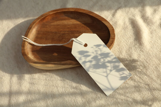 White blank sale tag in tray on fabric background with natural sunlight