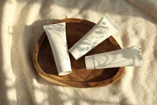 White plastic cream tubes in tray on fabric background with natural sunlight. Beauty concept
