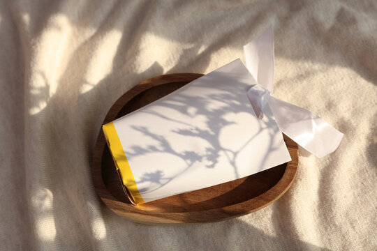 CArdboard pack with bow in tray on fabric background with natural sunlight. Beauty concept