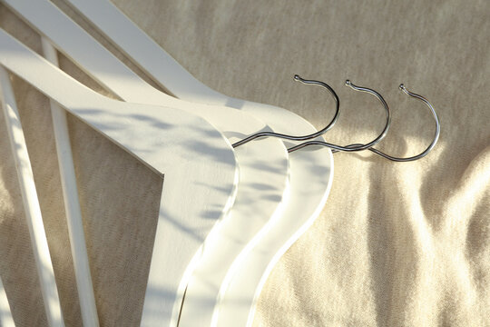White hangers on a fabric background with sunlight. Fashion, shopping concept.