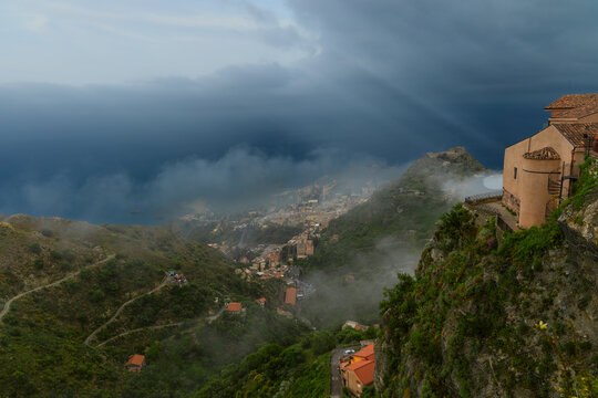 Aerial panorama dramatic mountain village overlooking the sea under a stormy cloudscape sun shine beams epic scenery view