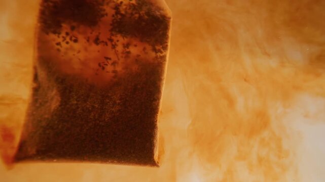 Tea bag steeping in hot water releasing color and flavor into clear liquid motion.