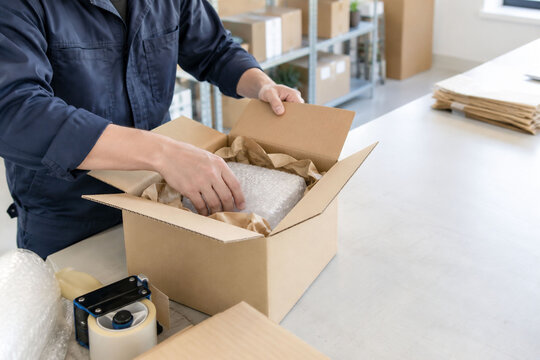 物流倉庫で緩衝材を使い段ボール箱に商品を丁寧に梱包する日本人男性スタッフの発送業務
