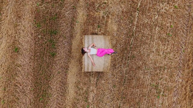 Top down drone view reveals a woman resting on a hay bale as camera rises above