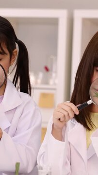 Schoolgirls in Lab Coats Examining Plant Stem with Magnifying Glass