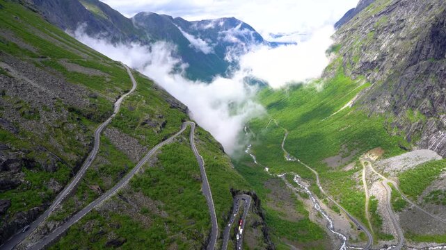 Spectacular serpentine road winding through lush green Norwegian valley with flowing clouds.