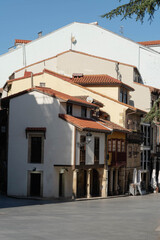 Terracotta tiled roofs and wooden glazed balconies top traditional stone houses on an old town square in Aviles, Spain. Vernacular architecture anchors heritage tourism and European travel themes. © Renata