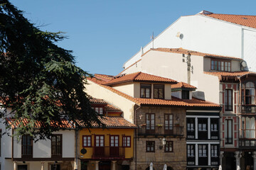 Terracotta tiled roofs and wooden glazed balconies top traditional stone houses on an old town square in Aviles, Spain. Vernacular architecture anchors heritage tourism and European travel themes. © Renata