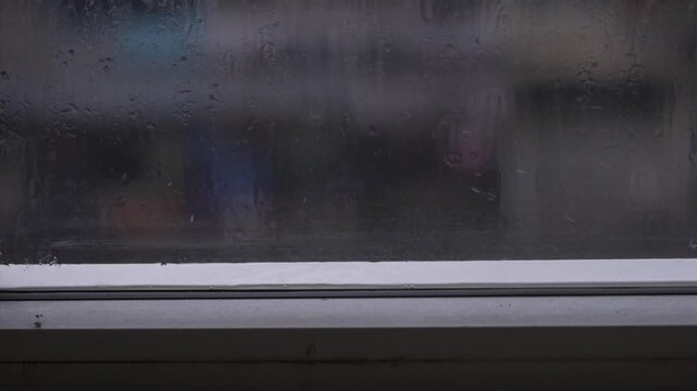 Raindrops and water condensation streaming down a clear window glass on a cloudy rainy day, creating a peaceful, moody, and cozy atmosphere
