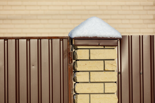 Brown fence with snow on top of brick pillar
