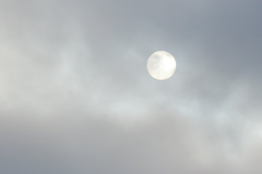 Pale sun shines through soft, drifting clouds. Gentle light filters through wispy, gray formations. Sky appears hazy, soft, and tranquil.