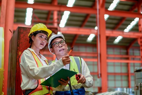 Technician teamwork coaching metal sheet machine system brainstorming project in manufactory Senior Male supervisor showing direction to female engineer with clipboard and radio transceiver