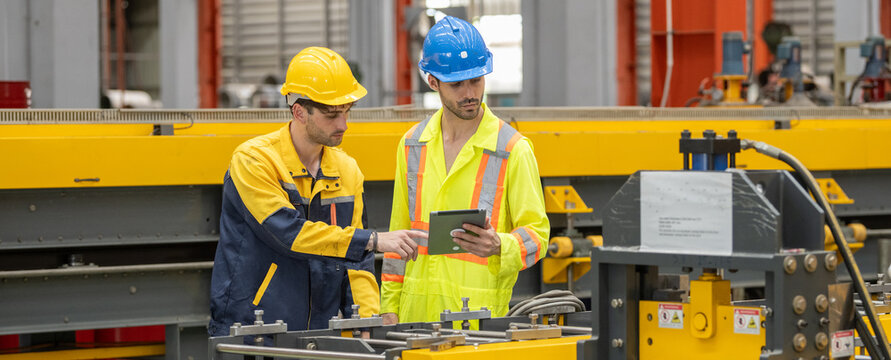 Engineers team inspecting metal sheet machine system inspection check collaboration in factory Two male workers wear safety helmet discussing operational data on tablet at manufacturing factory