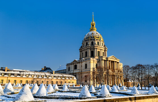 The gilded dome of Hotel des Invalides and snow covered topiary garden under a clear blue sky in winter in Paris, France.