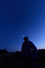 Silhouette of a person in nature observing night sky, Moon, stars and planets from a remote location. © astrosystem