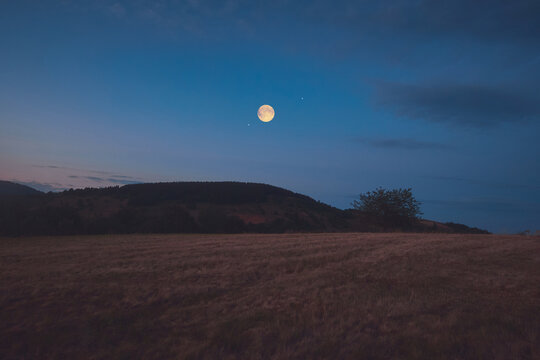Full Moon, stars and planets above landscape silhouettes in blue hour time.