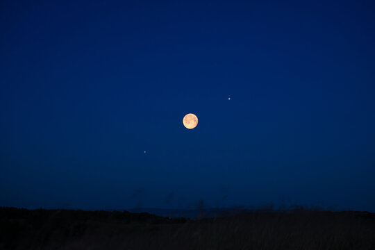 Full Moon on a twilight sky with landscape silhouettes.