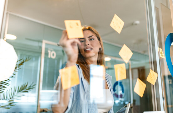 Agile project management. Sticky notes and strategy planning, Business brainstorming and teamwork concept. Young businesswoman organizing task notes on a glass office partition wall.