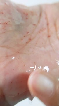 Clear glossy gel with raspberry extract reflecting light on palm skin. Gel being spread evenly using finger. Skincare texture concept for beauty treatment.