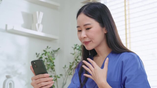 Close-up of an Asian nurse holding a phone and speaking to remind a patient to take their medication dose during a remote consultation.