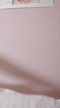 Soft shadows move across smooth light pink painted wall with subtle texture. piece of medical diagram is partially seen at top right corner. At bottom soft folds suggest presence of white