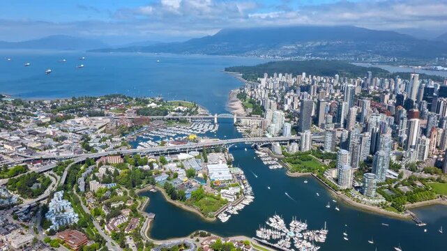 Scenic drone shot overlooking Vancouver's False Creek and marina waterways, with downtown skyscrapers, coastal bridges, and North Shore mountains in view.
