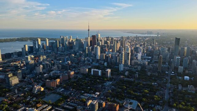 Aerial drone shot of the downtown Toronto skyline and CN Tower illuminated by golden hour sunlight, overlooking Lake Ontario and the financial district.