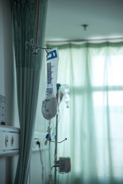 A bag of milky white intravenous nutrition solution hangs on the IV stand, with various facilities in the hospital ward in the background.