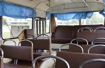 Interior view of an empty retro bus with brown leather seats and blue curtains on the windows © Nazar