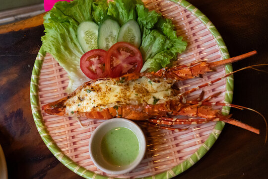 A Deliciously Grilled Lobster Dish Served with Fresh Vegetables and Spicy Dipping Sauce Presented on a Bamboo Platter