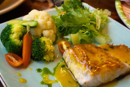 A Deliciously Plated Dish Featuring Succulent Fish, Fresh Vegetables, and Vibrant Greens on a Colorful Restaurant Plate