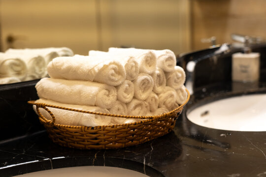 Neatly Arranged White Towels in a Woven Basket on a Elegant Bathroom Countertop, Complementing a Polished Vanity Surface with Modern Design
