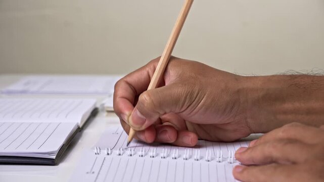 Hand gripping pencil and writing essay on lined paper