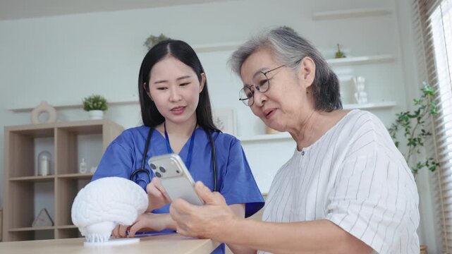 Elderly woman shows her phone to young nurse next to brain model on table, using digital brain training app for memory and cognitive care.
