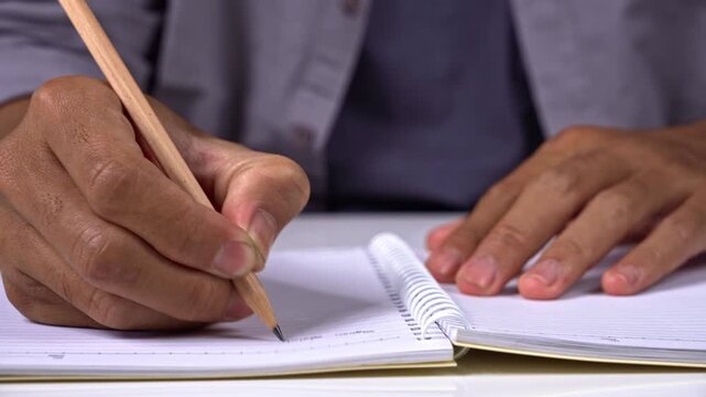 Student writing essay in spiral notebook with pencil