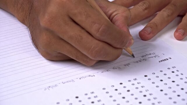 Student writing essay on exam paper with pencil
