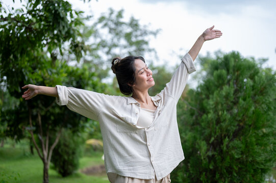 Asian woman stretching arms out joyfully in green outdoor nature setting.