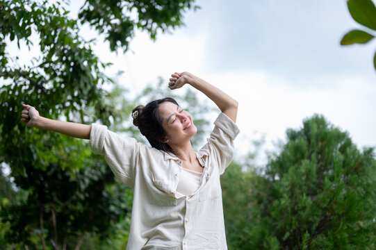 Asian woman stretching arms wide with joyful smile in outdoor nature.