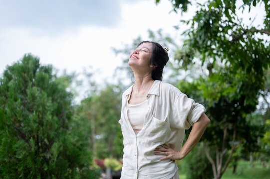 Asian woman smiling with eyes closed and hand on hip enjoying nature outdoors.