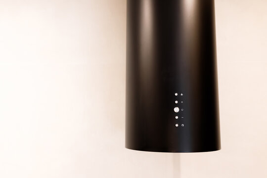 Close up shot of modern minimalist black cylindrical kitchen cooker hood range extractor with luminous led light controls, white wall background, sleek contemporary household appliance design