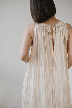 Back View Of Woman Wearing Cream Pleated Sleeveless Dress With Ribbon Tie