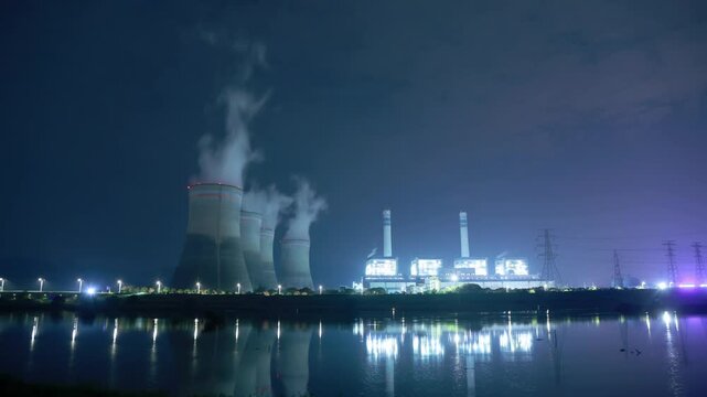 night view of power plant cooling towers and lights reflection on water surface