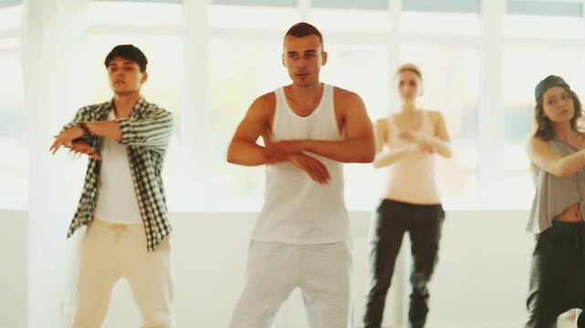 Young man standing performs basic hip hop movements in front of group of students. Developing precise movements, rehearsing arc elements, nae nae moving 
