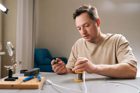 Skilled technician male soldering wires for repair, fixing cable connection with soldering iron, engaging in electronics hobby, preparing components for diy project, working on circuit board at home.