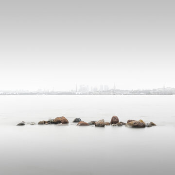 Minimalistische Langzeitbelichtung einer Steinmole in der Ostsee mit der Skyline von Tallinn, Estland im Hintergrund
