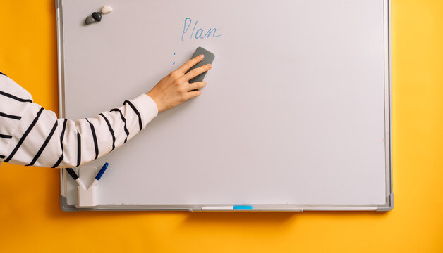 Hand wiping blue marks beneath Plan on a whiteboard with a gray eraser.
