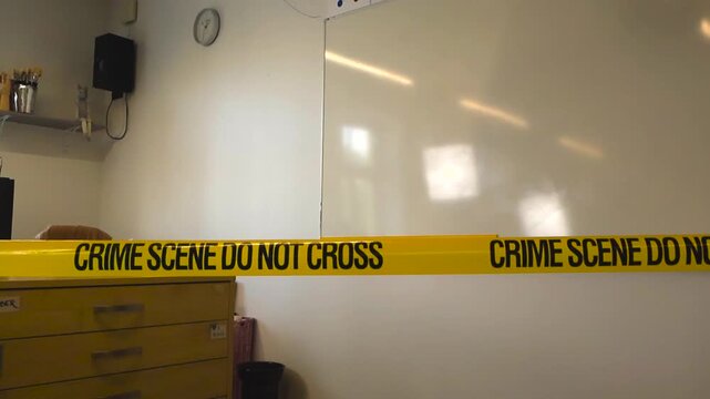 Yellow police tape with the warning Crime Scene Do Not Cross stretches across an empty school classroom, sealing off the area during an official investigation near a whiteboard and desk